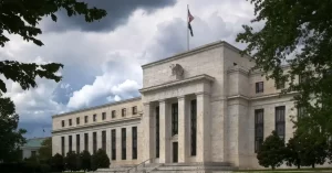The Federal Reserve building with American flag, framed by trees and dramatic clouds, showcasing its grand architecture.