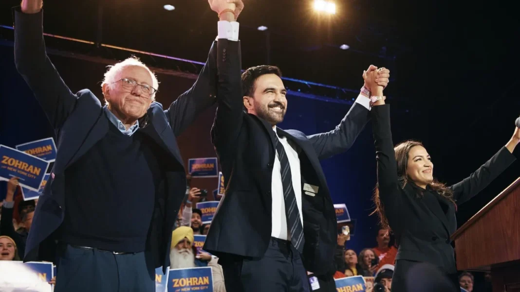 Socialists Take the Stage: Mamdani’s Far-Left Rally Shows How Deep the Democratic Divide Runs Bernie Sanders, AOC, and Zohran Mamdani raise hands at Queens rally as crowd chants “Tax the rich.