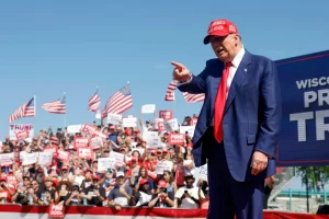 President Trump speaking at rally about cracking down on protest funders, waving American flags in background