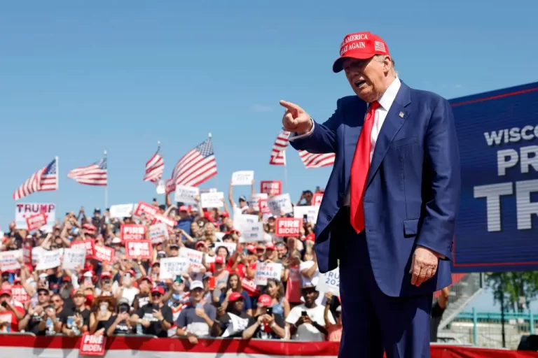 President Trump speaking at rally about cracking down on protest funders, waving American flags in background