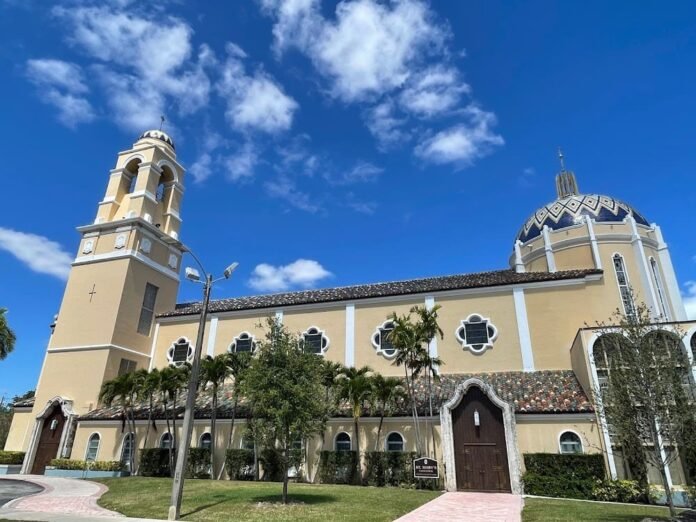 St. Mary's Church, featuring a tall tower and domed roof, surrounded by greenery under a bright blue sky with scattered clouds.