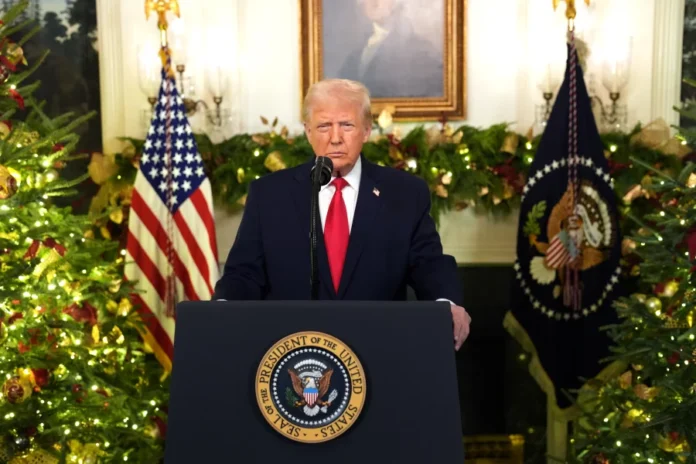 A person stands behind a podium with the presidential seal, surrounded by festive decorations and American flags.