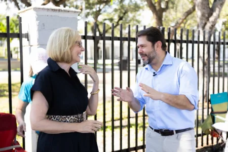 A man and woman are engaged in a lively conversation outdoors near a fence.