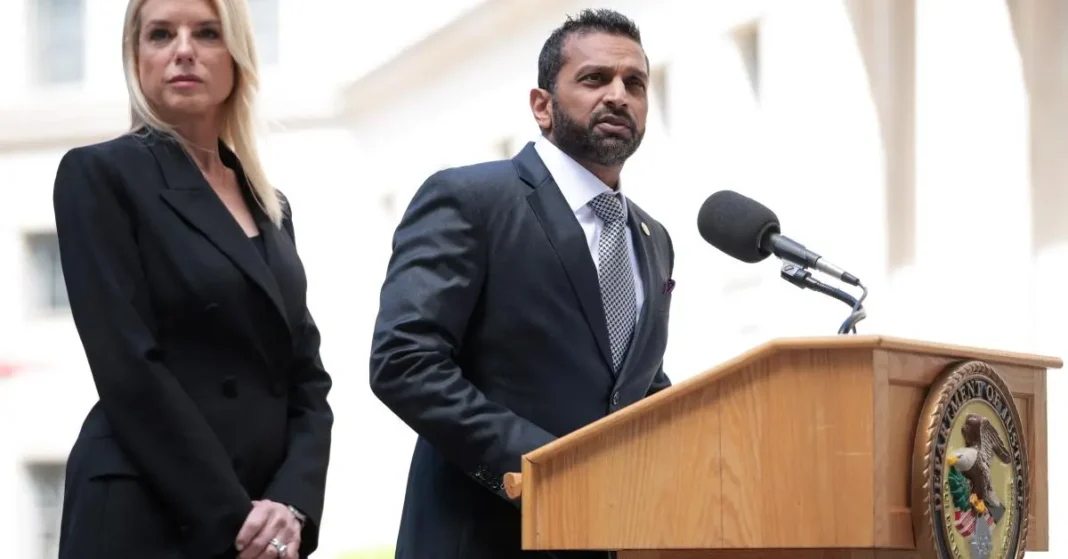 A man in a suit speaks at a podium with the Department of Justice seal, while a woman stands beside him in a black outfit.
