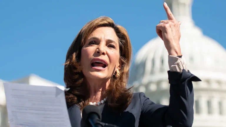 Maria Elvira Salazar Breaks With Trump, Blasts Immigration Pause as “Un-American” A woman speaks at a podium outdoors, holding papers in one hand and gesturing upward with the other, with a domed government building in the background.