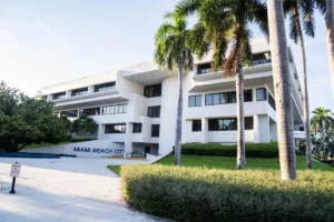 Miami Beach City Hall, a modern white building surrounded by lush greenery and palm trees, bathed in soft sunlight.