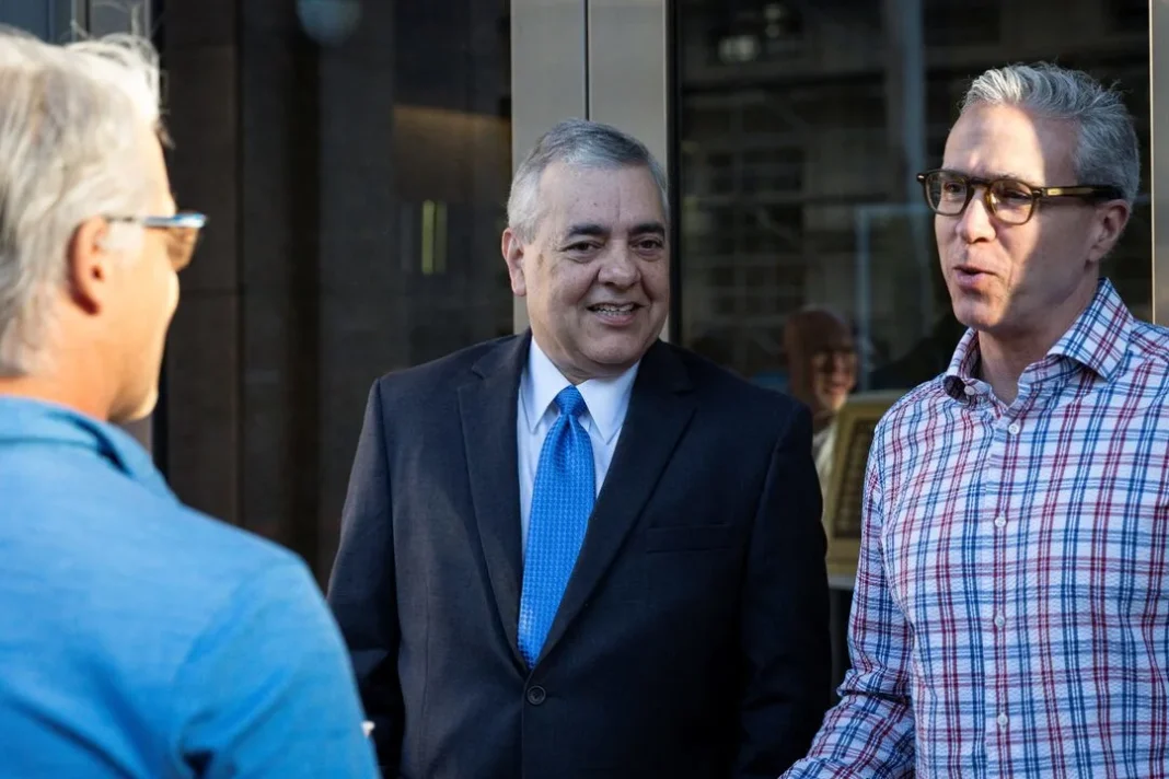 david-rivera-miami-court-bail-cash Three men having a conversation outside, one in a blue sweater, one in a suit with a blue tie, and one in a plaid shirt.