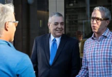 David Rivera’s Allies Offer Cash and Homes to Help Him Post Bail Three men having a conversation outside, one in a blue sweater, one in a suit with a blue tie, and one in a plaid shirt.