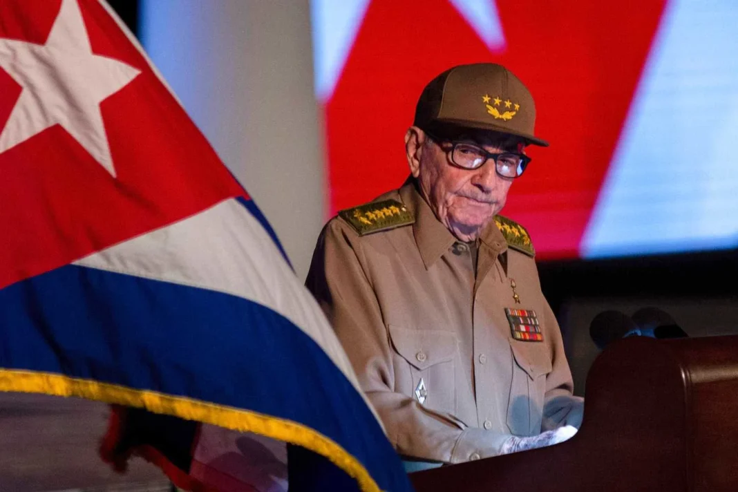 raul-castro-indictment-miami-2026 Military officer in uniform stands behind podium with Cuban flag in the foreground and a red and blue backdrop.