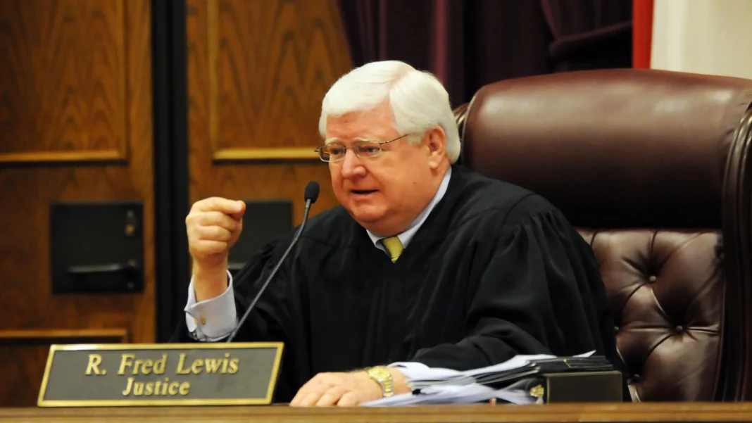Judge in black robe seated at bench with nameplate 
