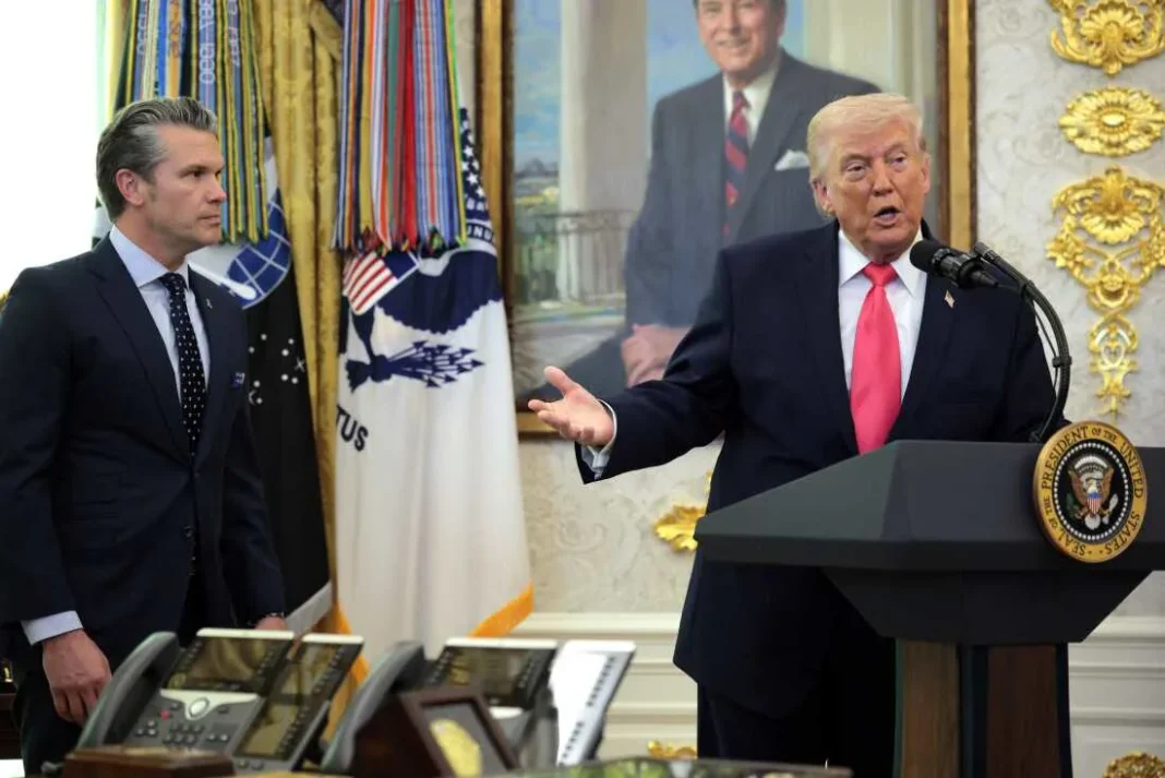 Trump Says He Is “In No Hurry” to Finalize Iran Deal as Nuclear Demands Remain Central A man in a suit speaks at a podium with the presidential seal, while another man in a suit stands nearby in a formal room with flags.