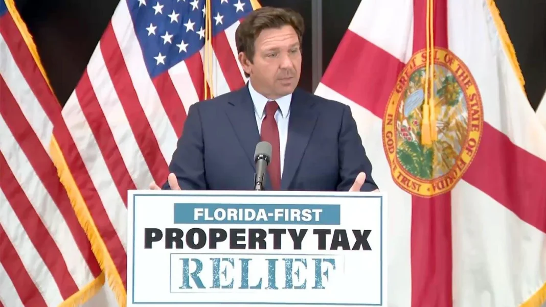 DeSantis Calls Special Session to Slash Property Taxes for Florida Homeowners Speaker at podium with "Florida-First Property Tax Relief" sign, standing in front of American and Florida state flags.