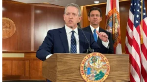 Former Florida House Speaker Paul Renner speaks at a podium while Gov. Ron DeSantis stands behind him during an official event in Florida.